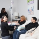 A friendly nurse with the IV Nurses administers IV hydration to a man and woman relaxing on a living room couch, illustrating the convenience of mobile IV therapy at home compared to traditional IV bars.