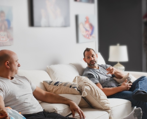 Two men on a couch receiving IV therapy with a visible drip, promoting vitamins for testosterone support.