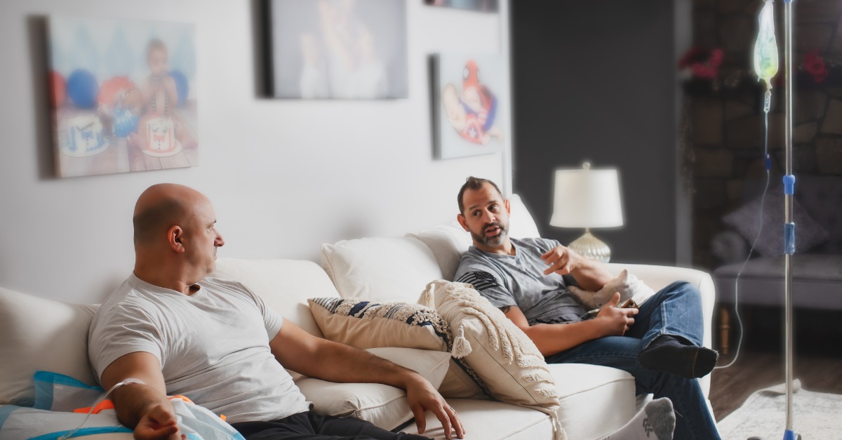 Two men on a couch receiving IV therapy with a visible drip, promoting vitamins for testosterone support.