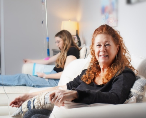 Two women receive IV therapy for hangovers in a comfortable living room setting.