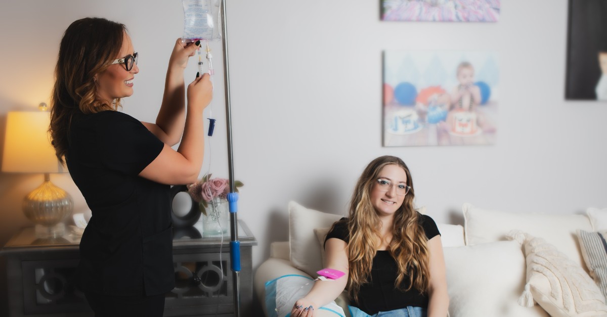 A woman is smiles while receiving iv infusion therapy for migraines from a healthcare professional.