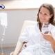 A senior woman in a white robe smiling while receiving IV vitamin therapy and holding a glass of water, illustrating wellness support for aging bodies.