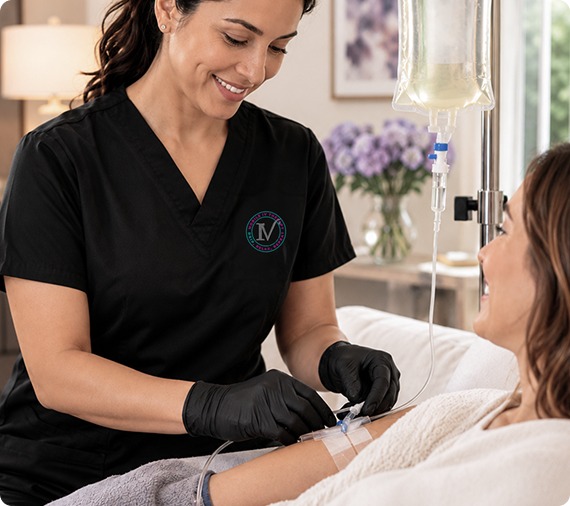 A nurse in black scrubs and gloves adjusts an IV line for a female patient receiving an infusion.